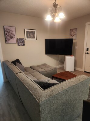 Ein Wohnzimmer mit einem Ecksofa, einem Flachbildfernseher, einer weißen Unterhaltungseinheit und Wandbildern.