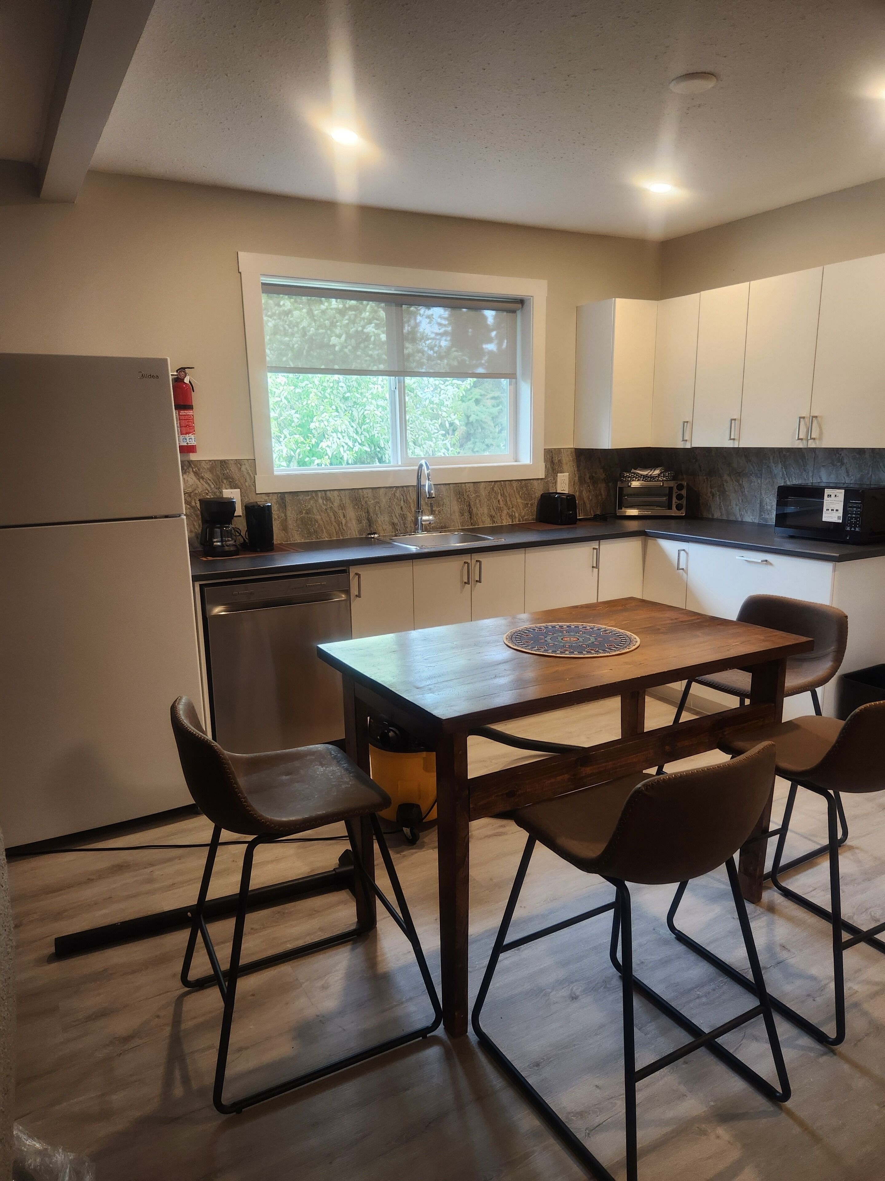 A kitchen with a wooden table, four chairs, a refrigerator, a sink, cabinets, and a window.