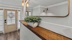 Un intérieur moderne avec un comptoir en bois, une plante en pot et un miroir qui reflète une porte et un luminaire.