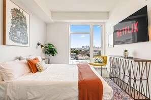 Une chambre d’hôtel avec un lit, un bureau, une chaise, une télévision, une plante et une vue sur la ville.