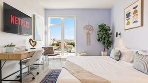 A modern bedroom with a bed, desk, chair, and a large window.