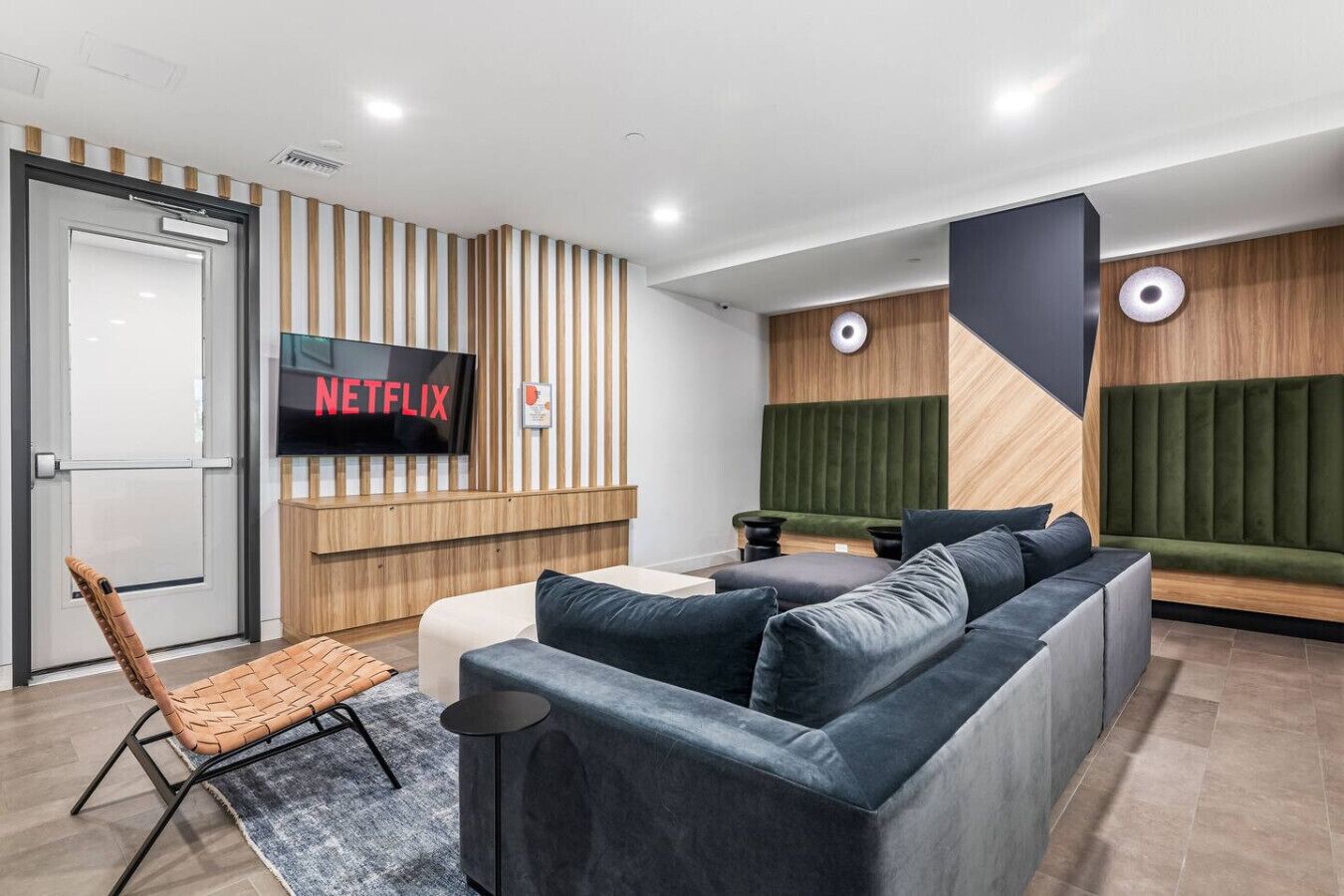 Un intérieur moderne avec un canapé d’angle, un écran de télévision affichant le logo « NETFLIX » et un mur décoratif en bois.