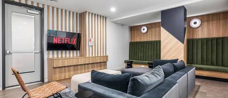 Un intérieur moderne avec un canapé d’angle, un écran de télévision affichant le logo « NETFLIX » et un mur décoratif en bois.