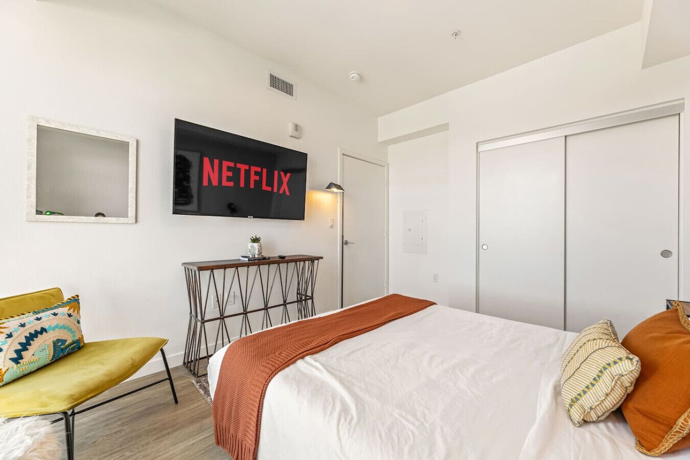 A hotel room with a bed, a TV mounted on the wall, a bedside table, and a chair.