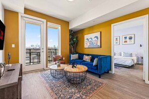 Ein modernes Wohnzimmer mit einem blauen Sofa, einem Couchtisch und Blick auf die Stadt durch große Schiebetüren.
