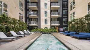 A pool area with lounge chairs and a water feature, surrounded by a building with balconies.