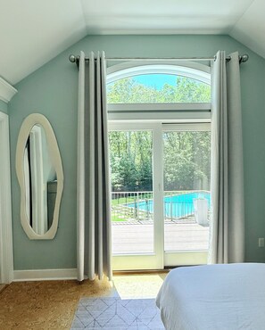 A bedroom with a large window, a bed, and a view of a swimming pool.