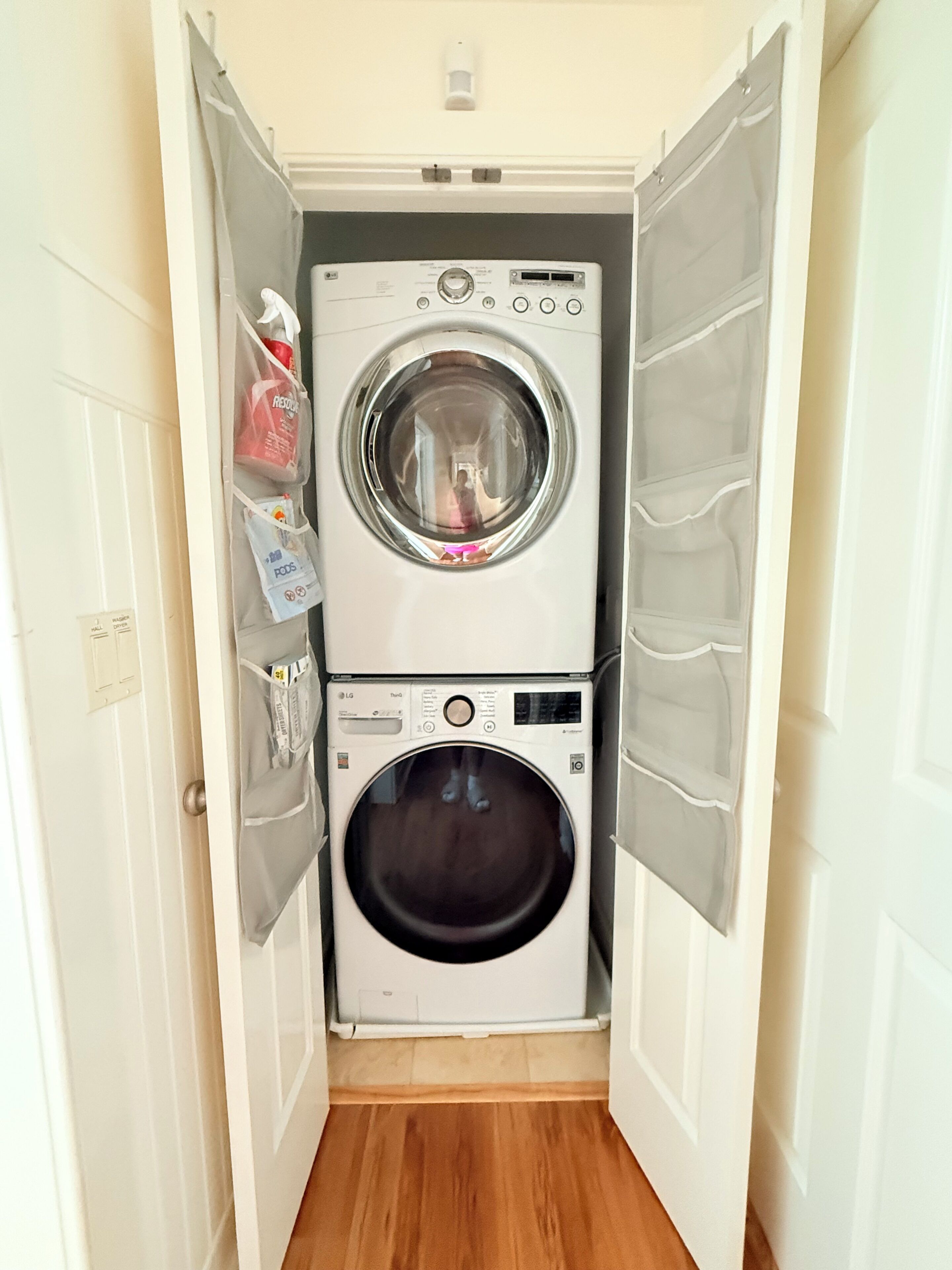 A compact laundry room with a front-loading washer and dryer, a small shelf with cleaning supplies, and a door with a light switch.