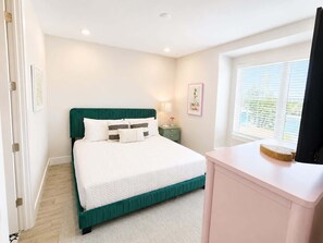 Un dormitorio con cama, mesita de noche, lámpara, cuadro y ventana.