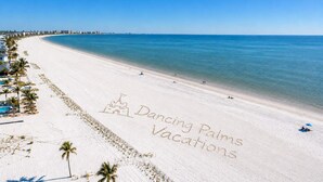 A beach with a clear sky, a palm tree, and the words 'Dancing Palms Vacations' etched into the sand. - Cabana Club · 4 Kings · 3 Min Beach (Fort Myers Beach)