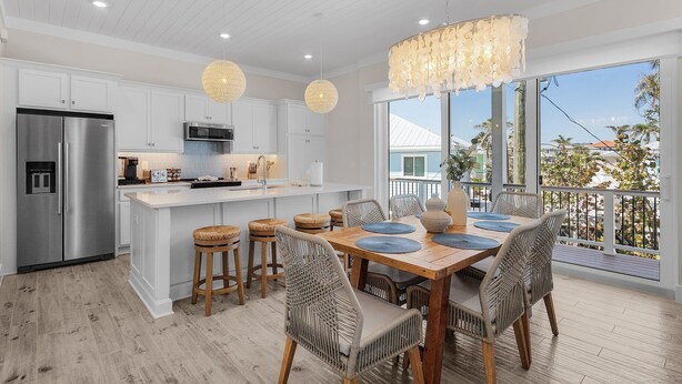 A modern kitchen with white cabinetry, stainless steel appliances, and a dining area with wicker chairs and a wooden table. - Cabana Club · 4 Kings · 3 Min Beach (Fort Myers Beach)