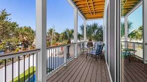 A wooden deck with a covered seating area, white railings, and a view of a swimming pool and greenery. - Cabana Club · 4 Kings · 3 Min Beach (Fort Myers Beach)