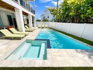 Una piscina con sillas de descanso, un jacuzzi pequeño y una cerca blanca.