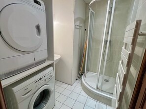 A compact bathroom with a washing machine, a toilet, and a glass-enclosed shower. - Les Tamaris: House with a view of the dunes, 5 minutes from the beach (Merlimont)