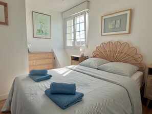 Quarto com cama, penteadeira, mesa de cabeceira, janela e obras de arte nas paredes.