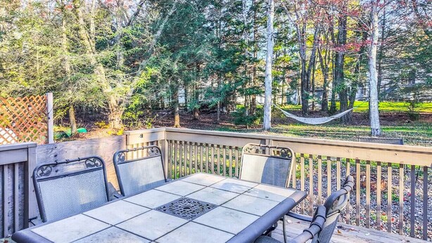 Une terrasse extérieure avec une table et des chaises, entourée d’une plateforme en bois et offrant une vue sur les arbres et un hamac.