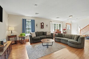 Ein Wohnzimmer mit einem Ecksofa, einem Couchtisch, einer Lampe und einer Uhr an der Wand.