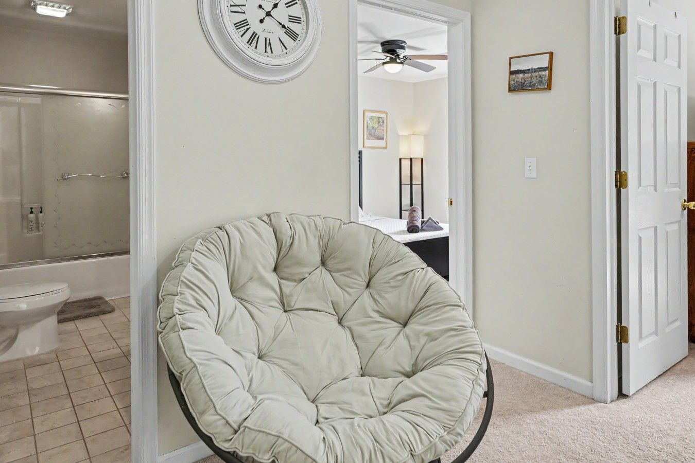 Una habitación con un sillón grande y redondo, una puerta blanca, un ventilador de techo y un reloj en la pared.