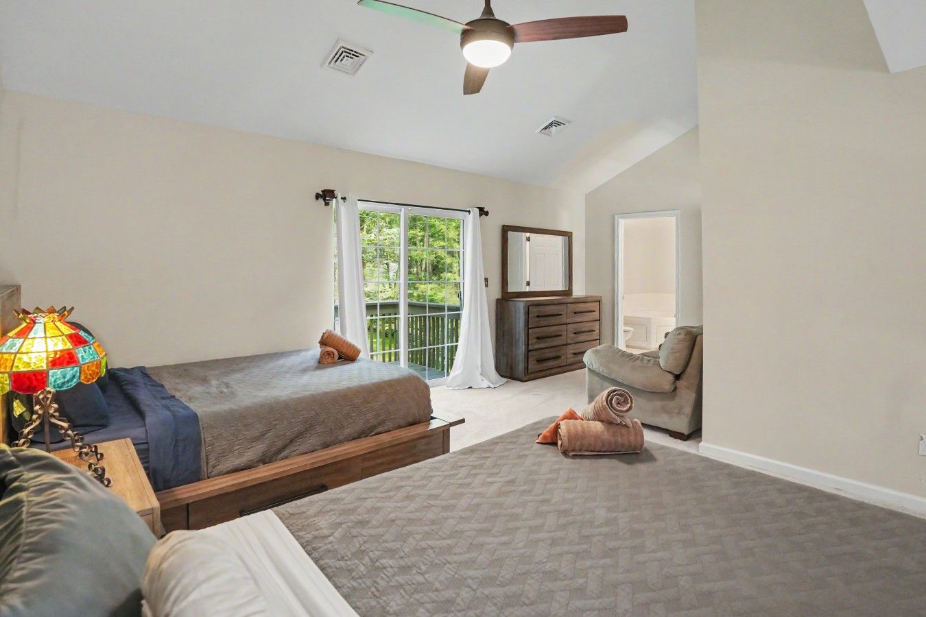 A bedroom with two beds, a dresser, a chair, a lamp, and a ceiling fan.