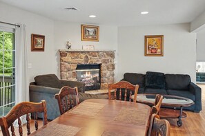 Ein Wohnzimmer mit Kamin aus Stein, einem Esstisch mit Stühlen, einer Couch und zwei gerahmten Bildern an der Wand.