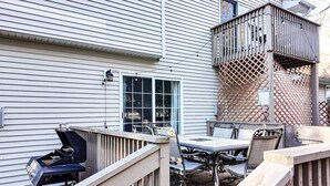 Une terrasse avec un barbecue, une table et des chaises, le tout entouré d’une clôture en bois.
