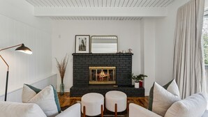 A modern living room with a fireplace, white walls, and a ceiling with wooden beams. - 3BR retreat w/ fireplace & BBQ grill (Lake Arrowhead)