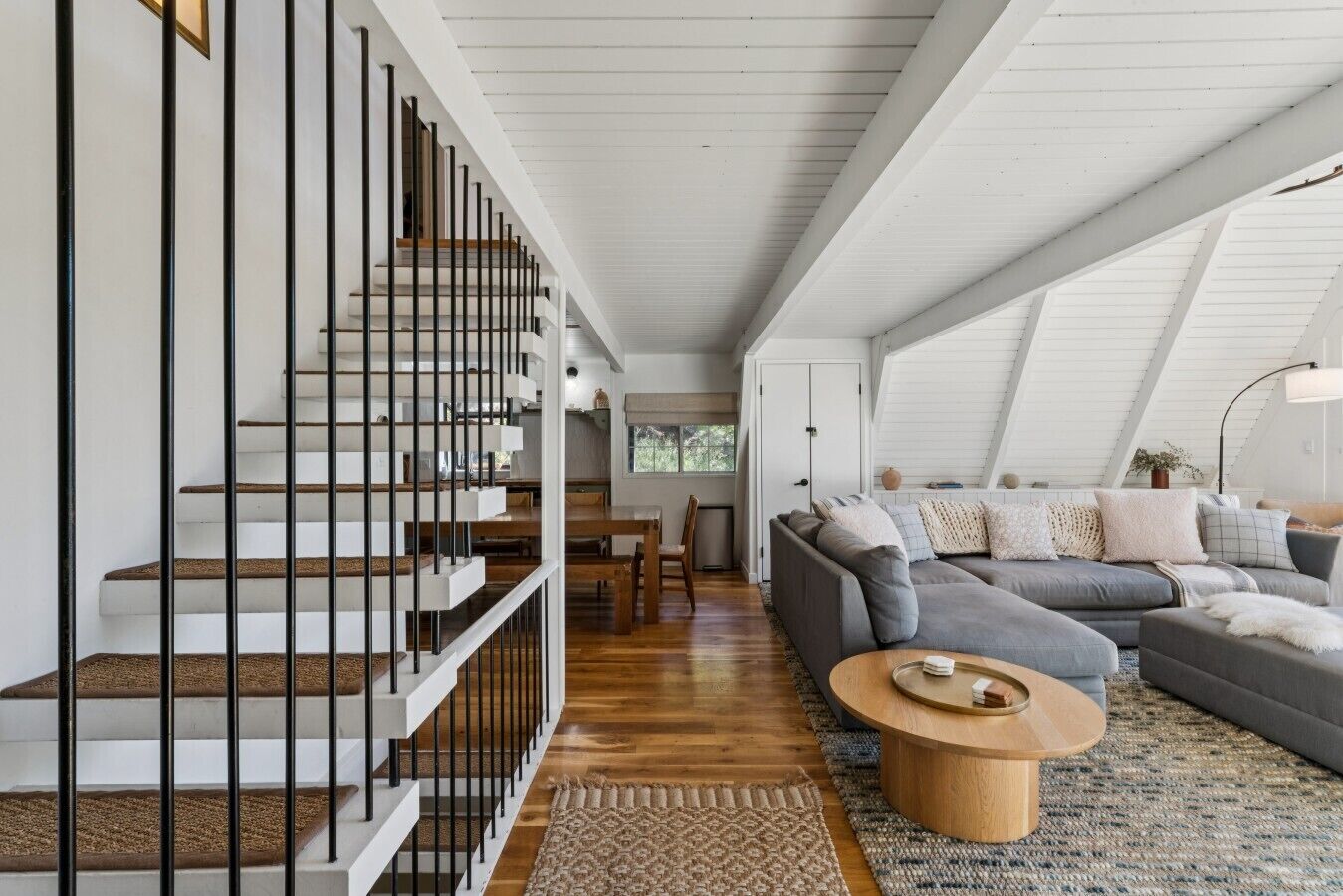 Un interior moderno con una escalera, una sala de estar con sofá y una mesa de comedor.