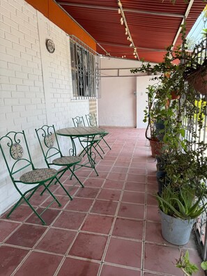 A covered patio with green metal chairs and a table, white brick walls, and potted plants. - Vive la experiencia de La Puebla Clásica en Casa Lu (Puebla)
