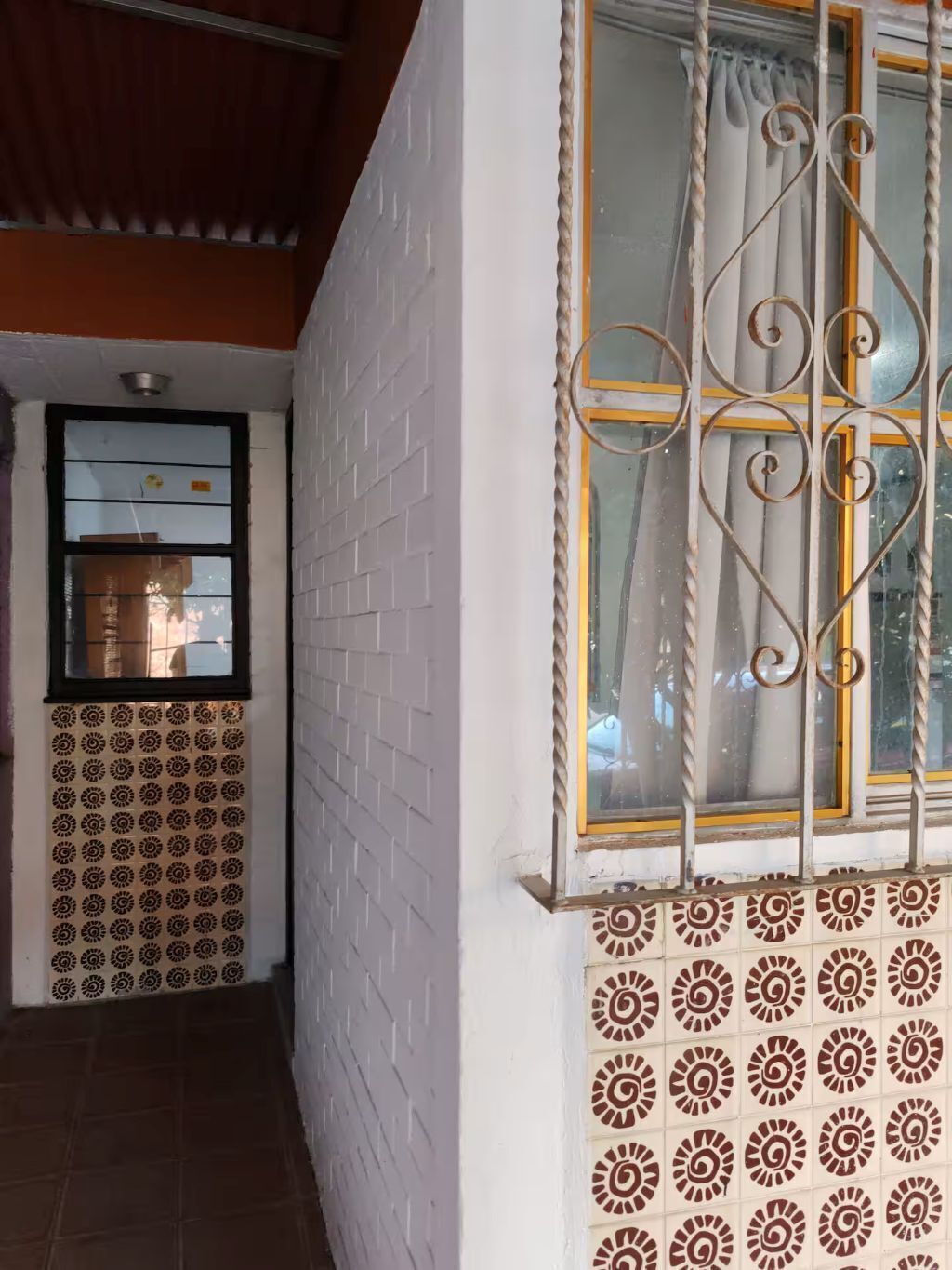 Ein Zimmer mit weißen Backsteinwänden, einem Fenster mit verzierten Metallgitterstäben und einem Fußboden mit Musterfliesen.