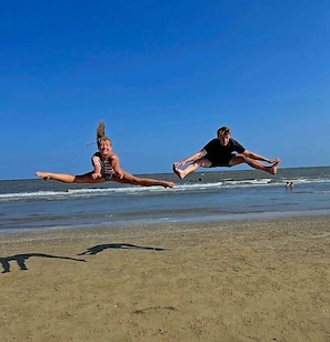 Zwei Personen in der Luft an einem Strand bei blauem Himmel.