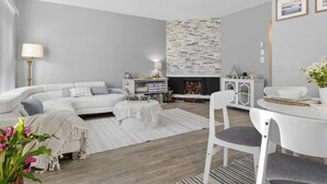 A modern living room with a white sofa, a dining table, and a fireplace with a stone accent wall. - Magical Monterey Carmel Pebble Beach travel, family and pet friendly whole Condo (Monterey)
