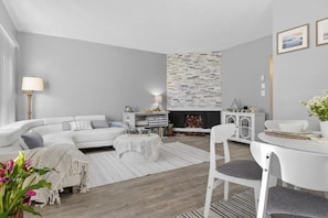 Ein modernes Wohnzimmer mit einem weißen Sofa, einem Esstisch und einem Kamin mit Steinwand.