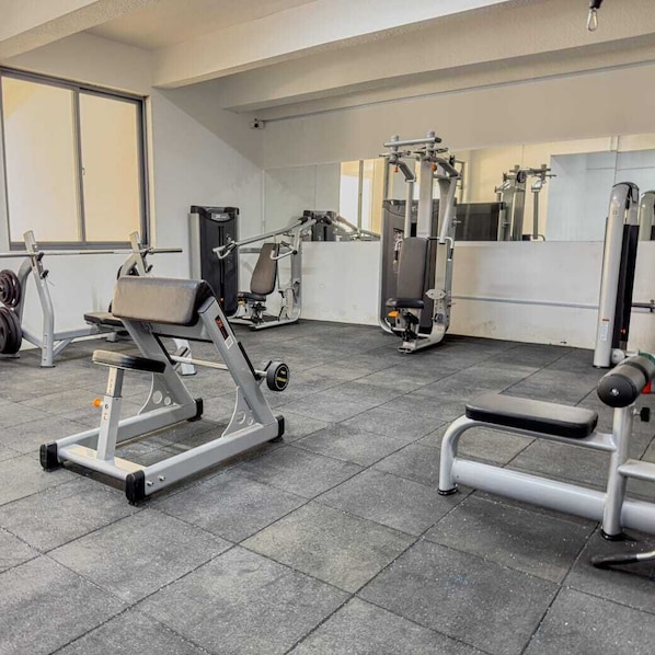 Ein Fitnessraum mit Krafttrainingsgeräten, Bänken und einer Spiegelwand.