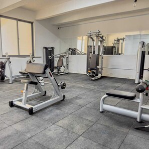 A gym with weight machines, benches, and a mirrored wall.