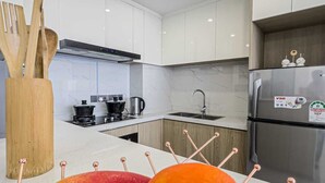 Una cocina moderna con armarios blancos, electrodomésticos de acero inoxidable y un frutero con manzanas y naranjas.