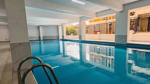 Una piscina interior con agua cristalina, una escalera metálica y suelo de baldosas.