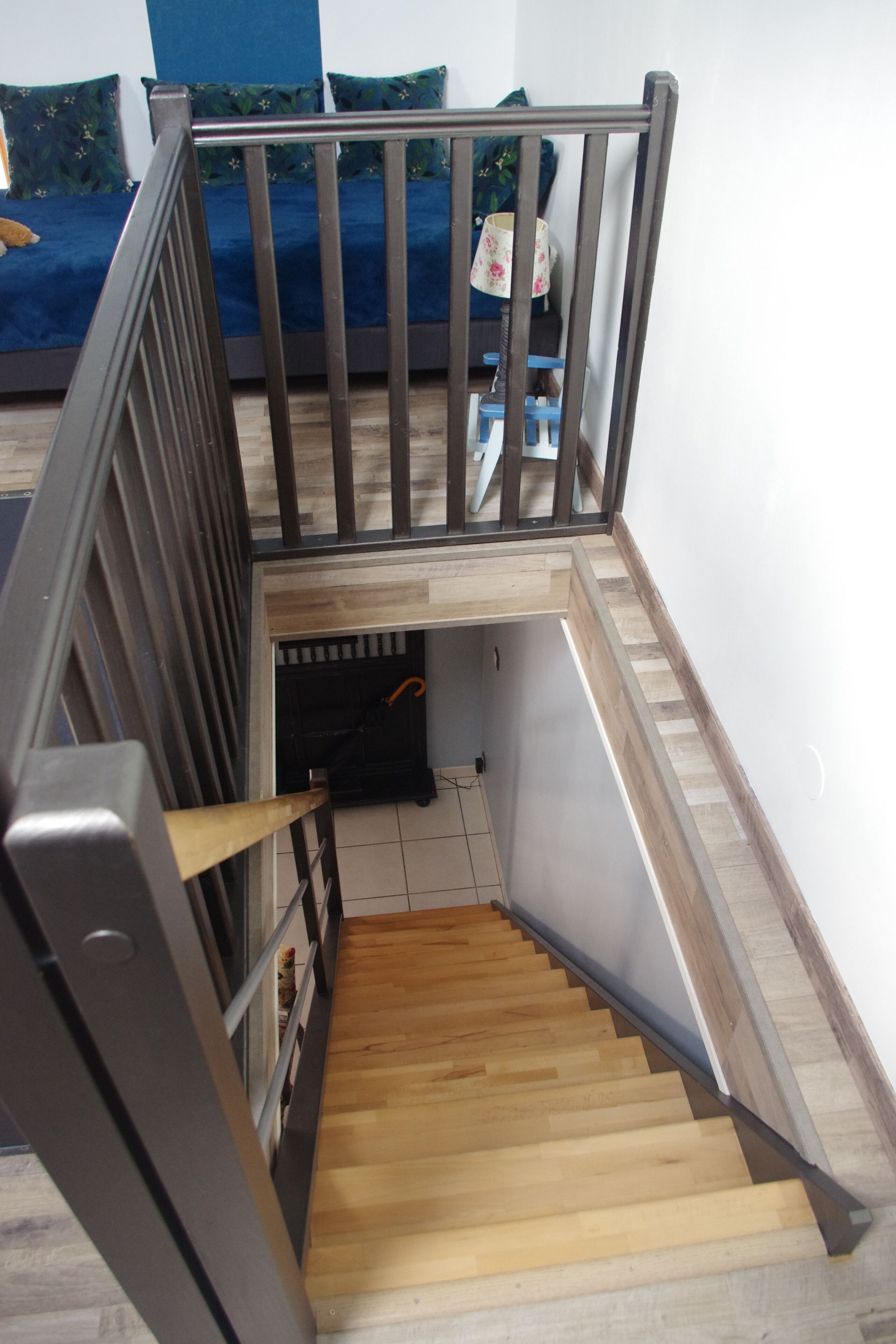 A wooden staircase with metal railings leading to a bedroom with a blue bedspread.