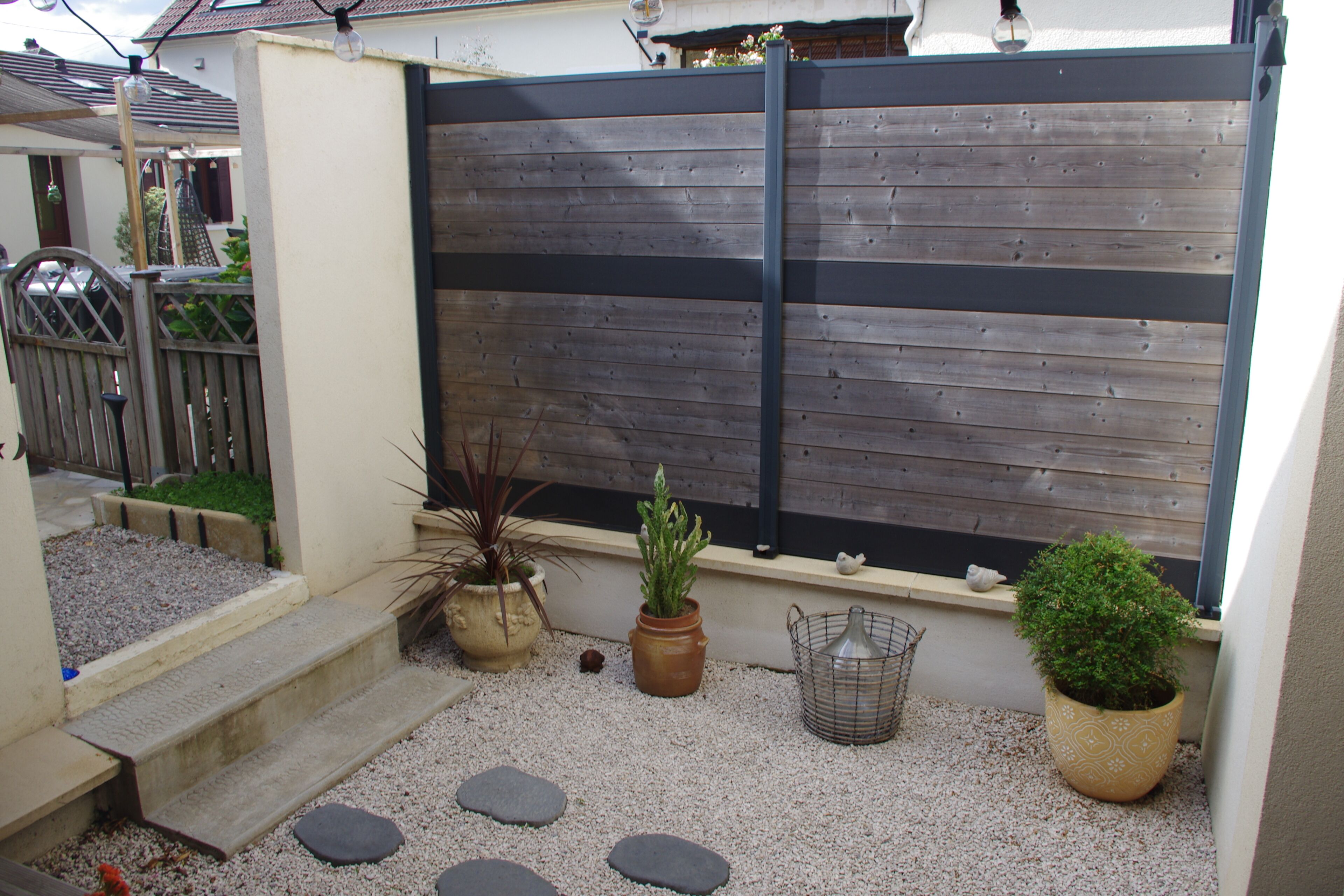 A garden with a wooden fence, steps leading to a door, and various potted plants.