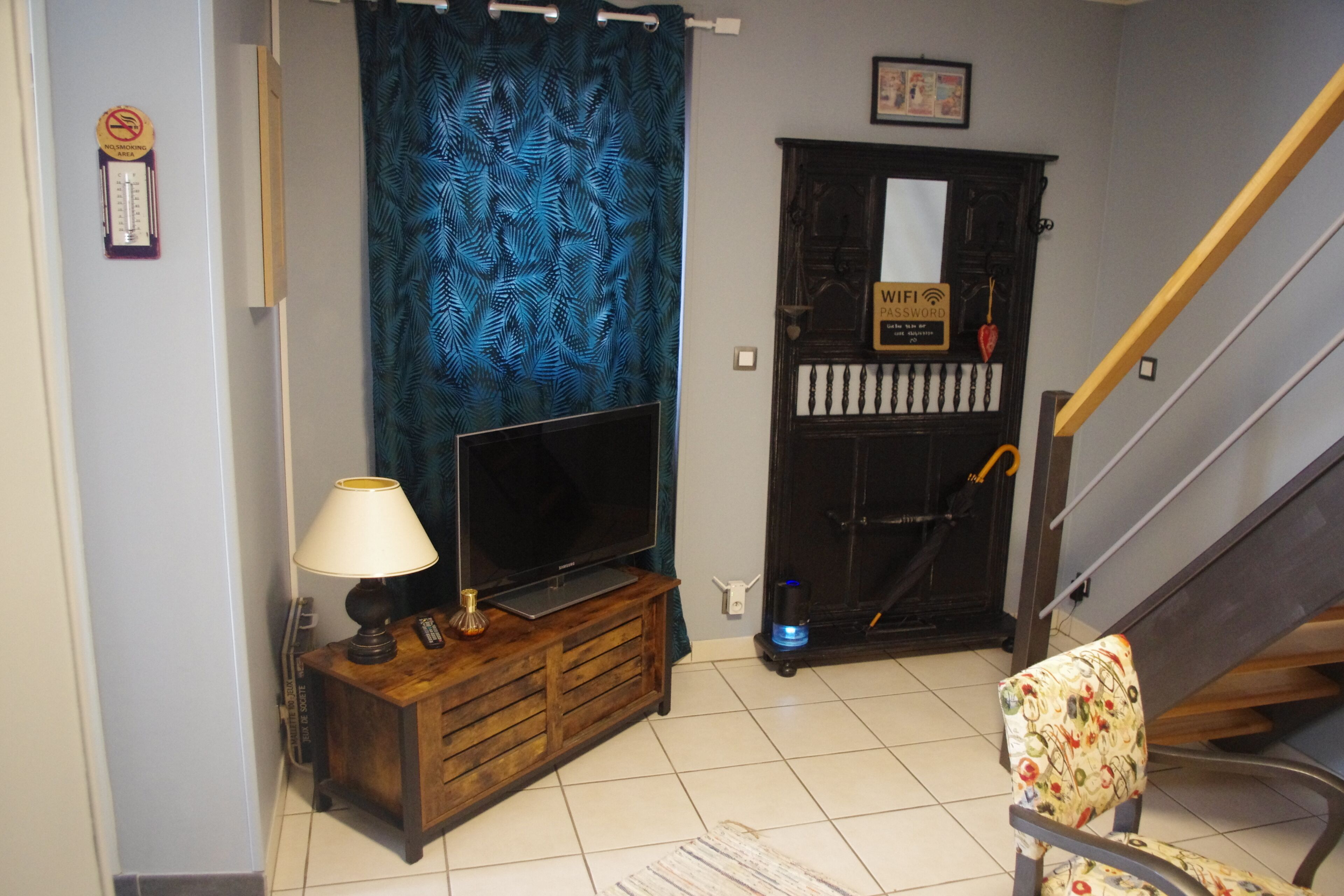 A living room with a TV, a lamp, a sofa, a blue curtain, a staircase, and a WiFi password sign.