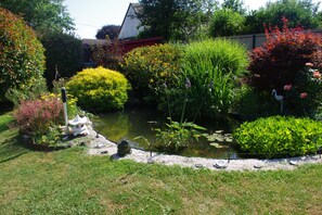 A garden with a pond, various plants, and a white birdhouse.