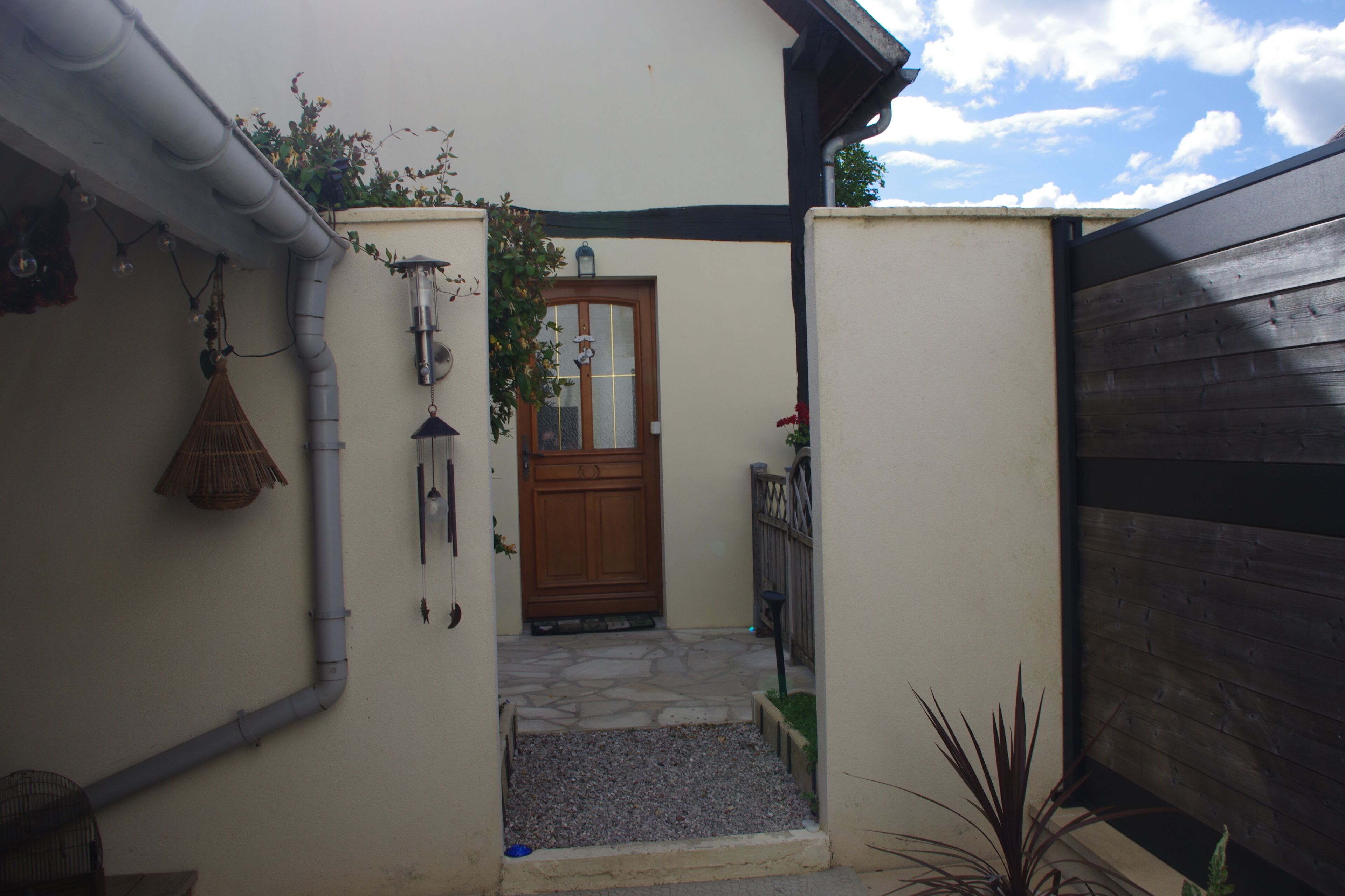 A narrow entrance to a building with a wooden door, a small step leading to a stone-paved area, and a metal gate to the right.