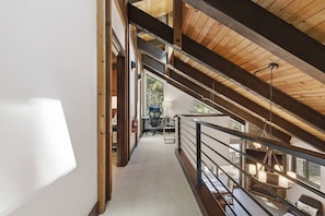 Ein modernes Interieur mit hoher Decke, Holzbalken, einer Treppe und einem Essbereich mit Tischen und Stühlen.