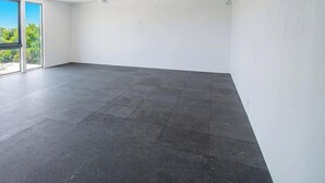 Ein geräumiger Raum mit dunklem Fliesenboden, großen Fenstern und weißen Wänden.