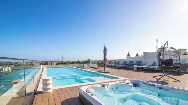 Ein Pool auf dem Dach mit Glasbarriere, Liegestühlen und einem Whirlpool.