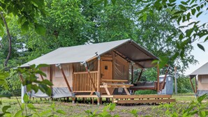 Una cabaña de madera con un porche cubierto, un pequeño espacio de estar al aire libre y un baño químico.