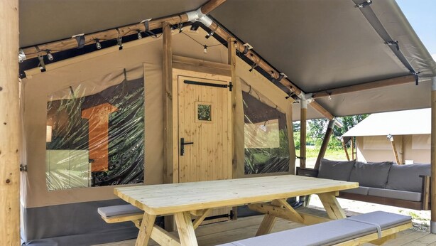 Une tente en bois avec une table et des bancs, une porte et un espace abrité.