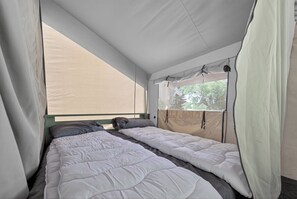 A tented accommodation with two beds, a window with a view of trees, and a mosquito net.
