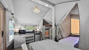 Un hébergement sous tente comprenant un coin cuisine, un lit et un luminaire suspendu.