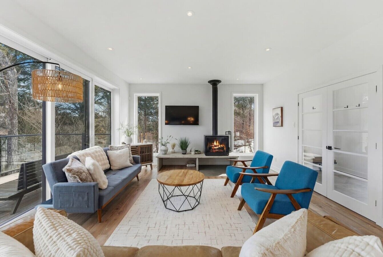 A modern living room with a fireplace, blue chairs, a sofa, and a large window.
