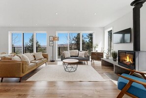 Ein geräumiges Wohnzimmer mit Kamin, großen Fenstern und einem modernen Sofa.